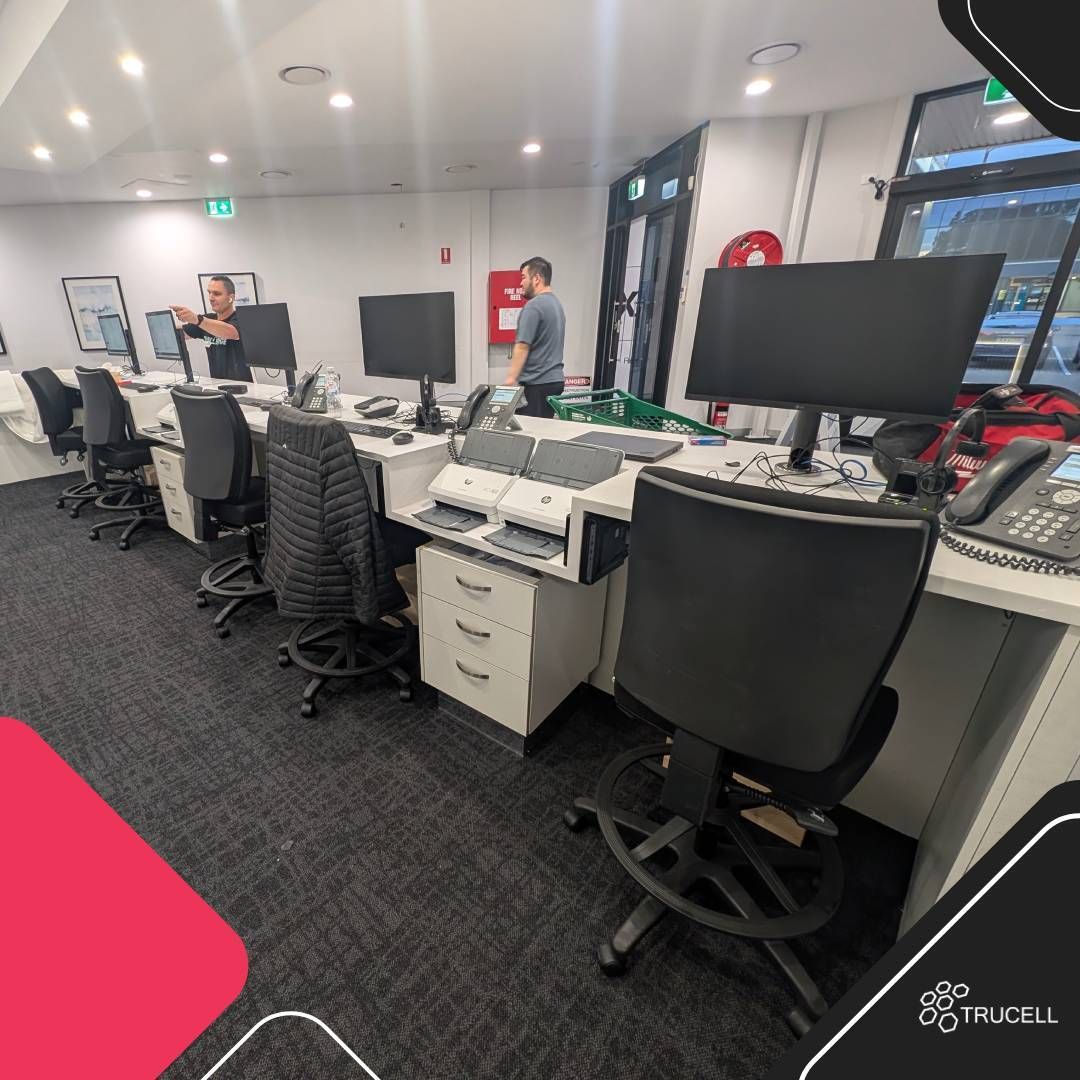 Front desk de Medical Imaging Erina ya implementado: estaciones de trabajo de recepción con dos monitores, escáneres HP, teléfonos VoIP 3CX, pedestales con cajones y personal configurando la línea durante la puesta en marcha